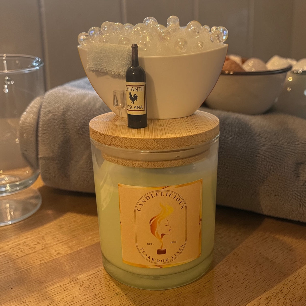 Teakwood Linen candle with a bubble bath and a bottle of red wine on the lid, photographed at home