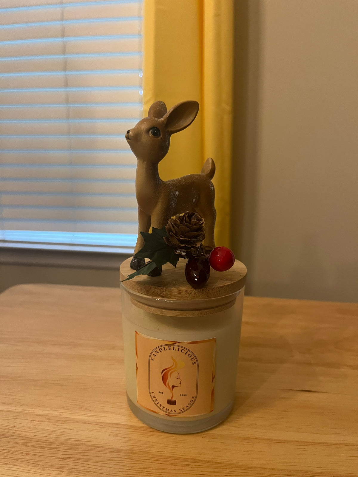 Christmas Season candle with a standing fawn beside a pinecone and holly on the lid