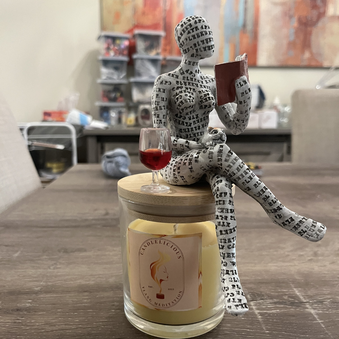 Ylang Meditation candle with a figure reading a book beside a glass of wine on the lid