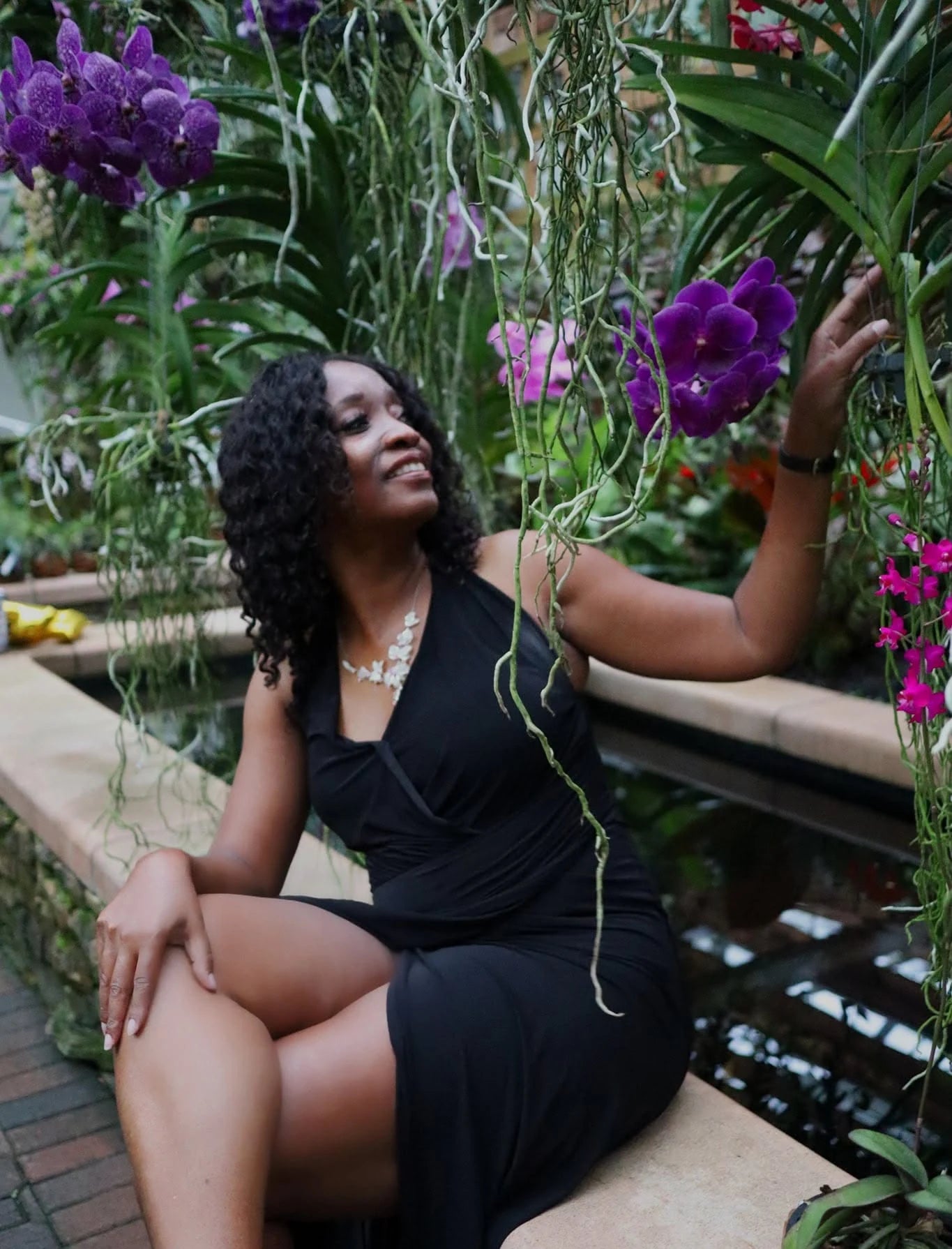 Sherrie sitting in a garden, reaching up to a purple orchid
